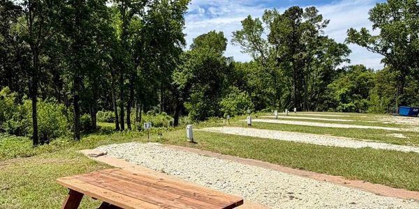 Sunny campsite with picnic table and numbered spots surrounded by trees.