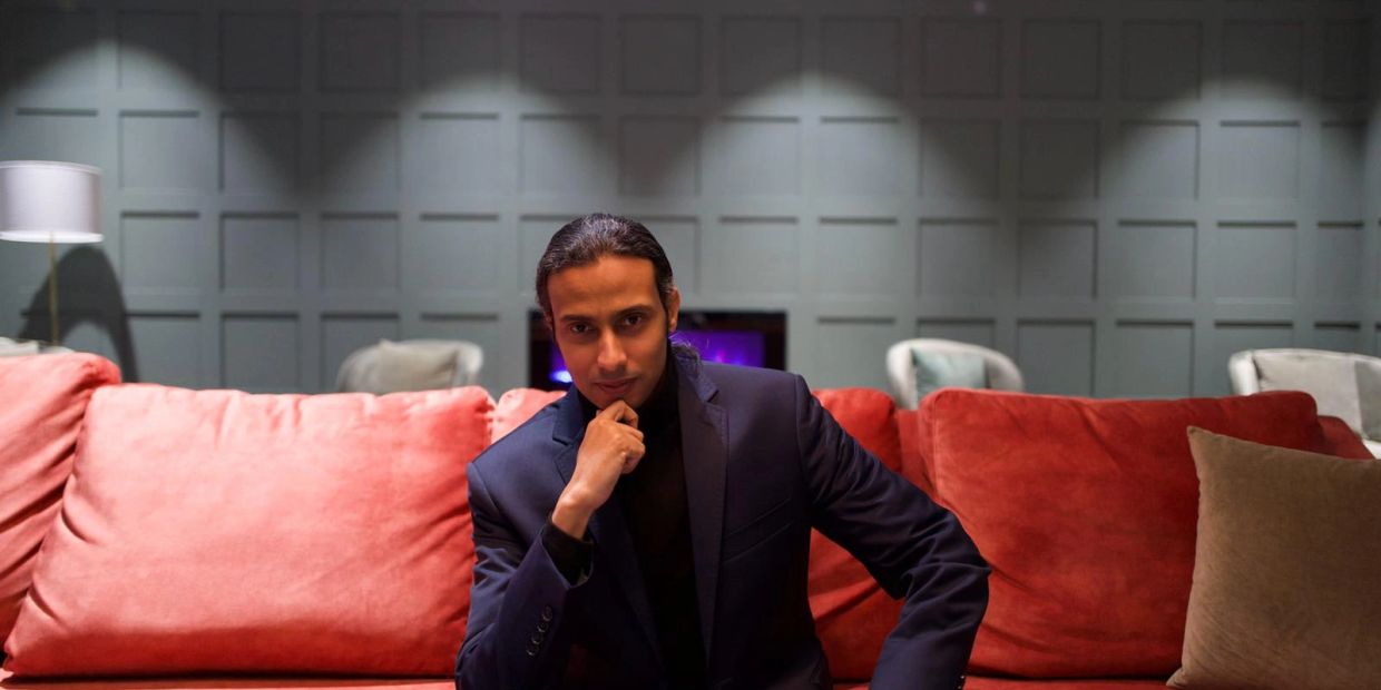 Man in a suit sitting on an orange couch thoughtfully.