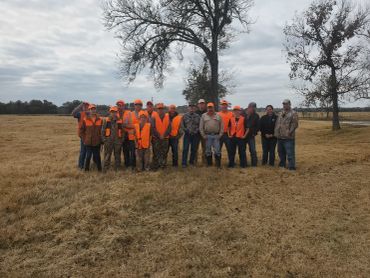 Group of hunters in orange gear standing in a field under cloudy sky.