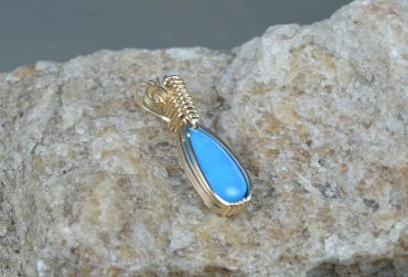 Blue stone pendant with gold wire wrapping on rock.