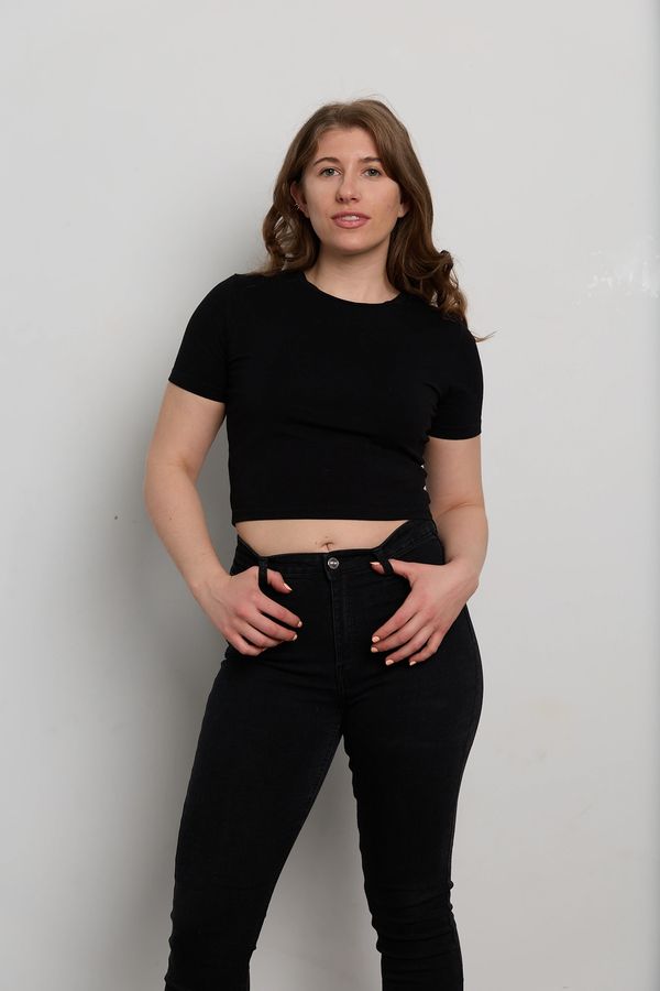 A woman in black crop top and jeans posing confidently against a plain wall.