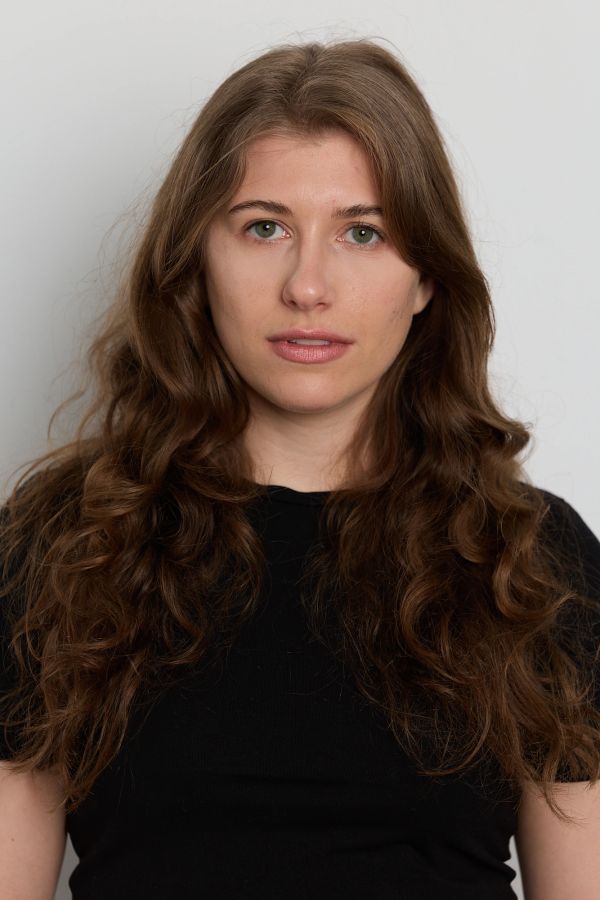 Young woman with long wavy hair wearing a black shirt, looking directly at the camera.