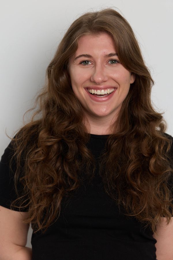 A joyful woman with long curly hair smiling brightly in a black shirt.
