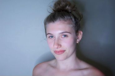 Woman with hair in a bun against plain background.