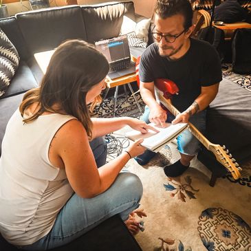 Two people discuss music notes with a guitar.