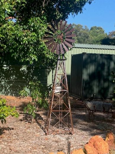 Rusty windmill in a garden near green sheds.