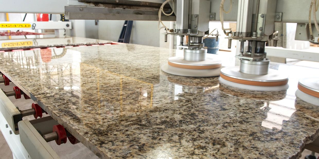 Machine polishing a granite slab to a smooth, shiny finish in a workshop.