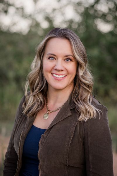 Smiling woman with wavy blonde hair outdoors in casual attire.