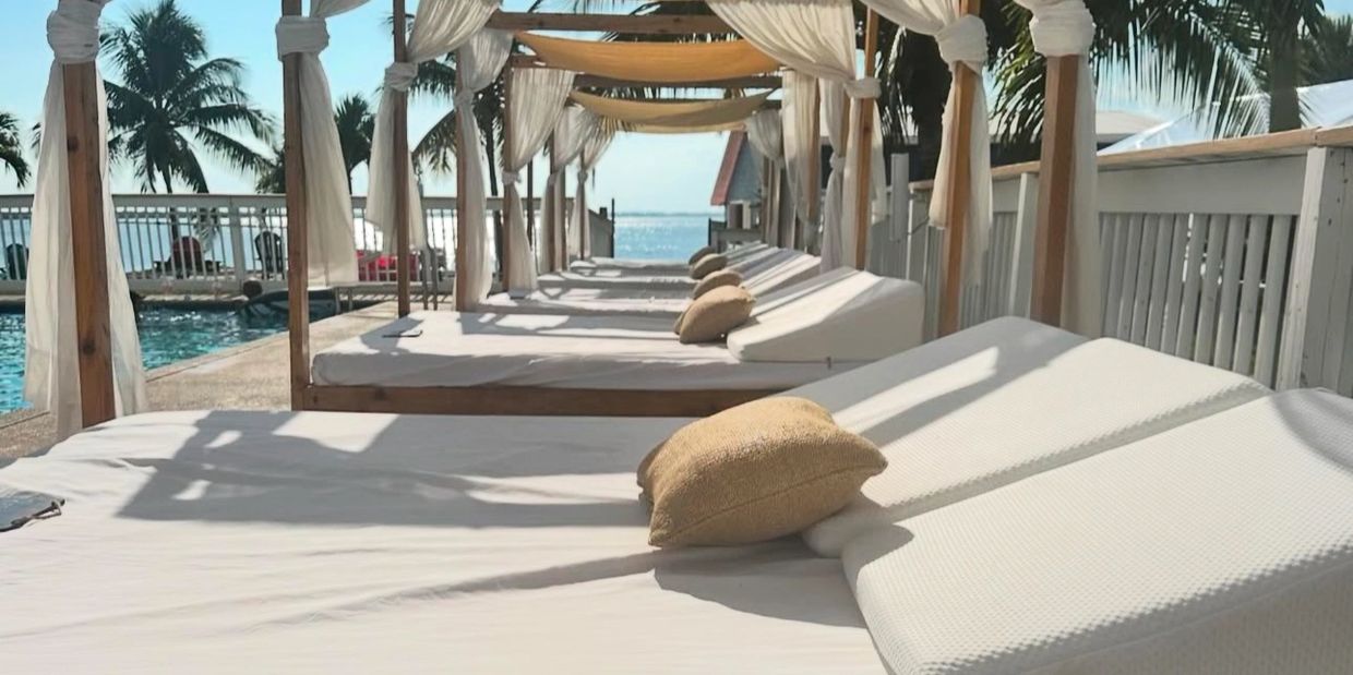 Beautiful wooden cabana beds with white tule curtains and surrounded by palm trees on Banana River