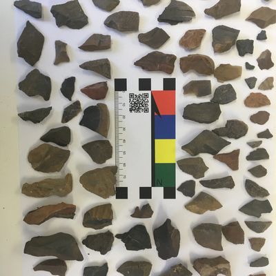 A collection of variously shaped stone fragments arranged around a color scale and ruler.