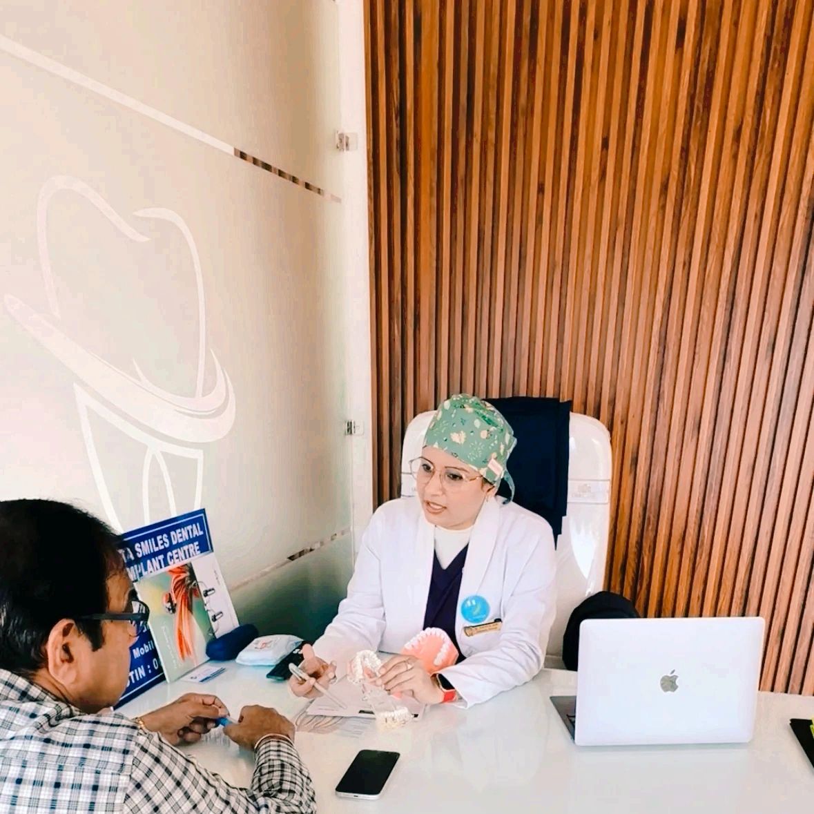 Dentist consulting a patient with dental models on the desk.