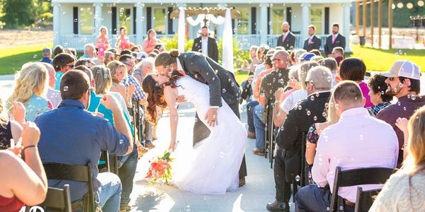 Bride and groom share a romantic kiss outdoors surrounded by guests and bubbles.