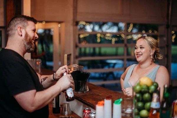 A bartender opening a beer bottle while a smiling woman watches.
