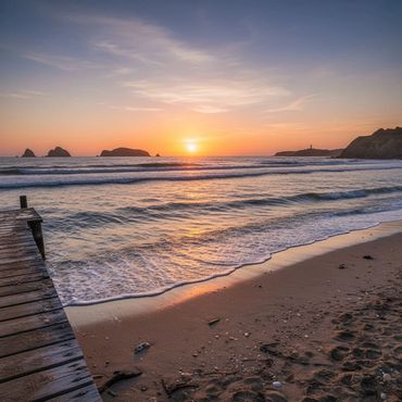 Sunset over a calm beach with gentle waves and a wooden pier.