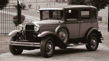 A vintage black and white classic car parked on a gravel driveway.