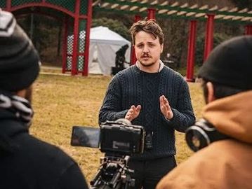 Man speaking to a camera crew outdoors.