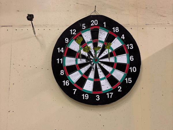 Dartboard on wall with several darts and a dart stuck in the wall.