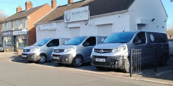 Three silver vans parked outside a white building under clear blue sky.