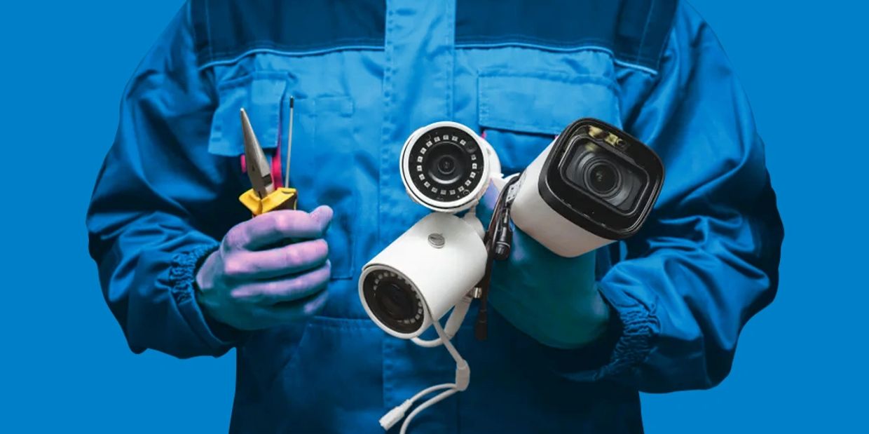 Technician holding security cameras and tools, ready for installation.