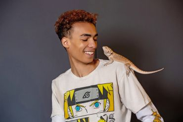 Young man smiling at a bearded dragon on his shoulder.