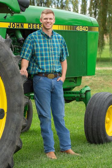 Man in plaid shirt standing by a green John Deere tractor.