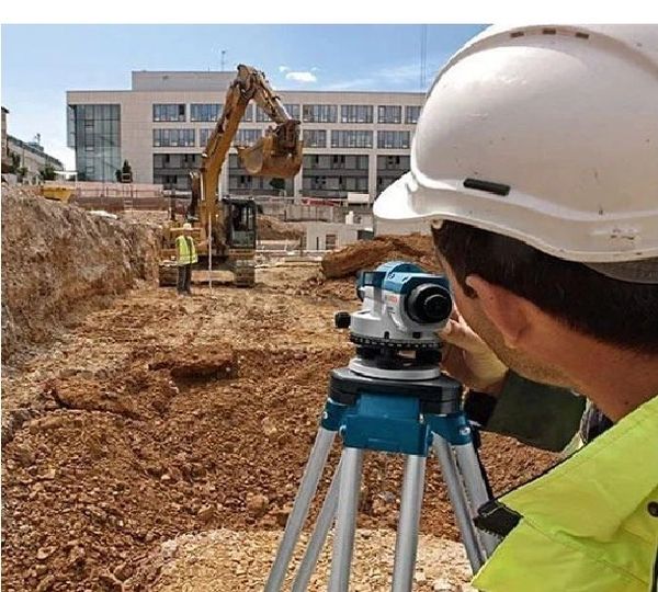 Construction worker surveying with equipment at excavation site.