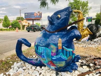 A colorful blue cat statue playing a saxophone on a roadside.