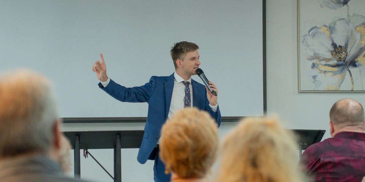 Man in blue suit giving a speech with a microphone.