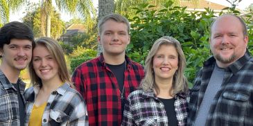 A happy family of five posing outdoors in plaid shirts.