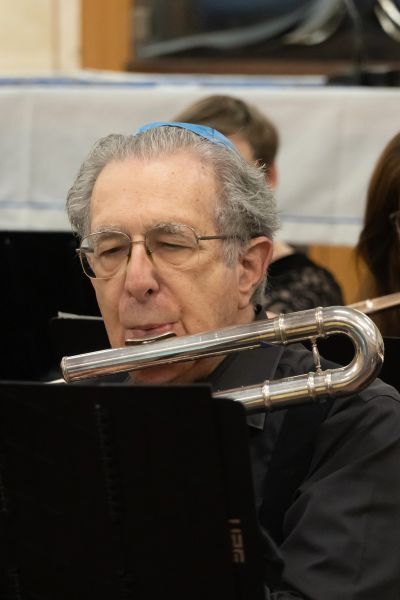 Elderly man playing a flute in an orchestra.