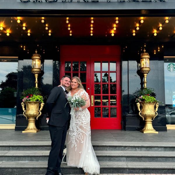 Newlywed couple poses happily outside Crowne Plaza with red doors and elegant decor.