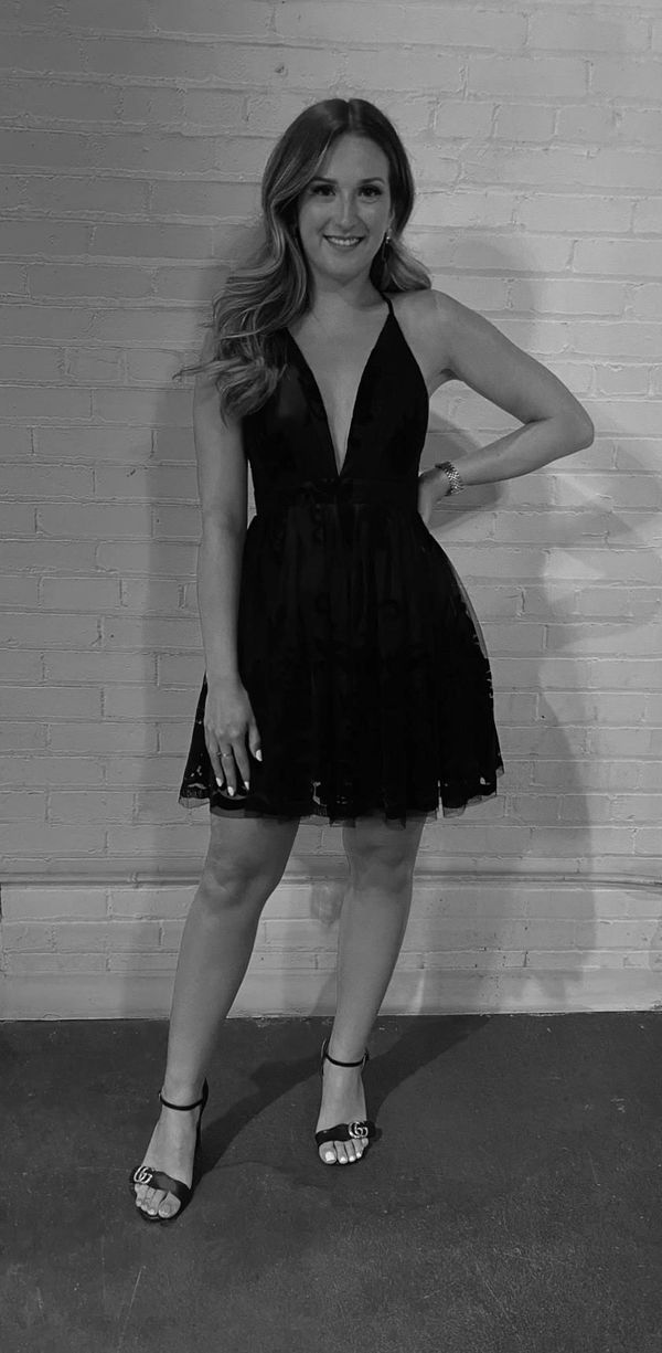 Woman in a black dress posing against a brick wall.