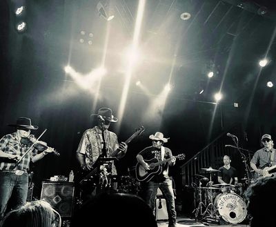 A band performs live on stage with various instruments and dramatic lighting.