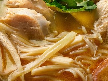 Close-up of a soup with chicken and enoki mushrooms in broth.