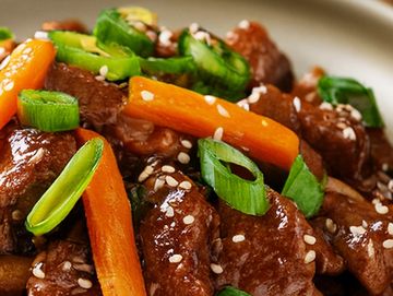 Close-up of stir-fried beef with carrots and green onions.