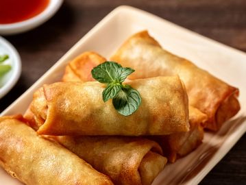 Golden fried spring rolls garnished with fresh mint on a rectangular plate.