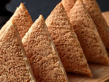 Close-up of sesame-coated triangular bread pieces arranged neatly.