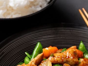 A plate of stir-fried chicken with vegetables and a bowl of white rice.