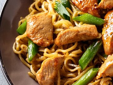 Stir-fried noodles with slices of cooked meat and green vegetables.