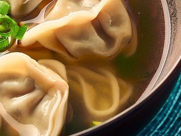 Close-up of dumplings in broth with noodles.