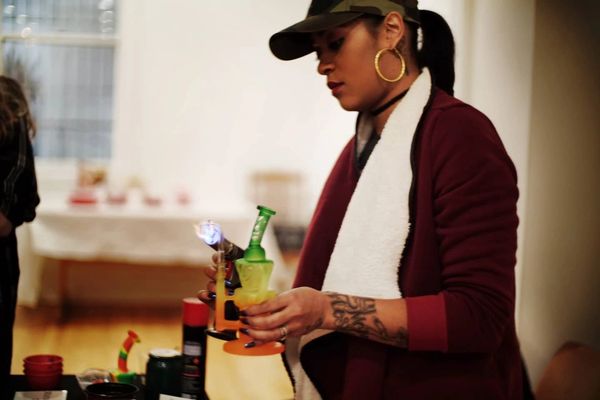 Woman holding a bong with a flame at a social gathering.