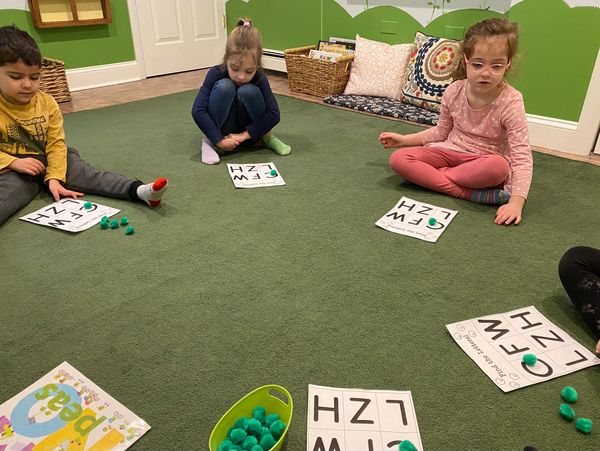 A group of children playing a literacy game on the rug, learning letter identification. 