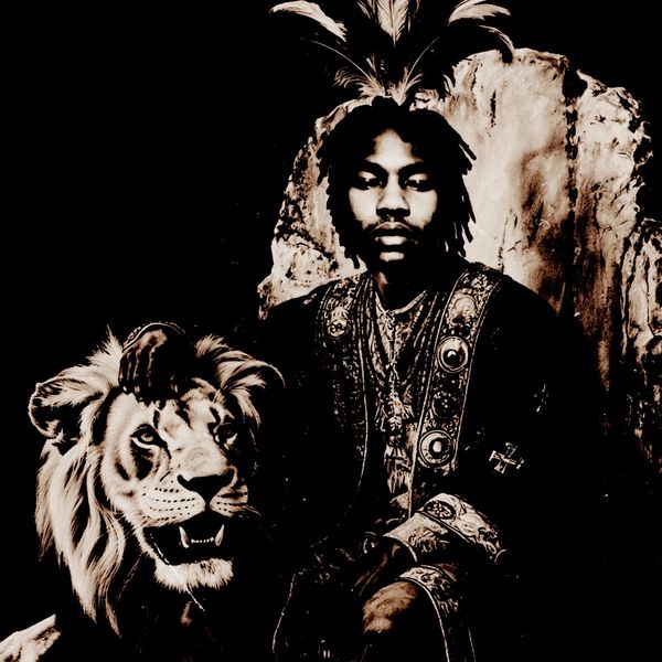 Man in ornate clothing with feathers on head, sitting beside a lion sculpture.