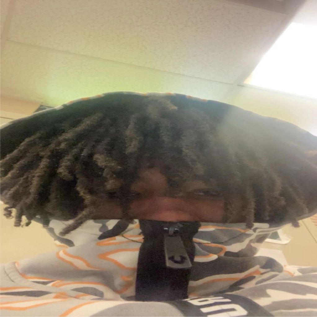 Person with dreadlocks wearing a zipped-up patterned hoodie covering their face.