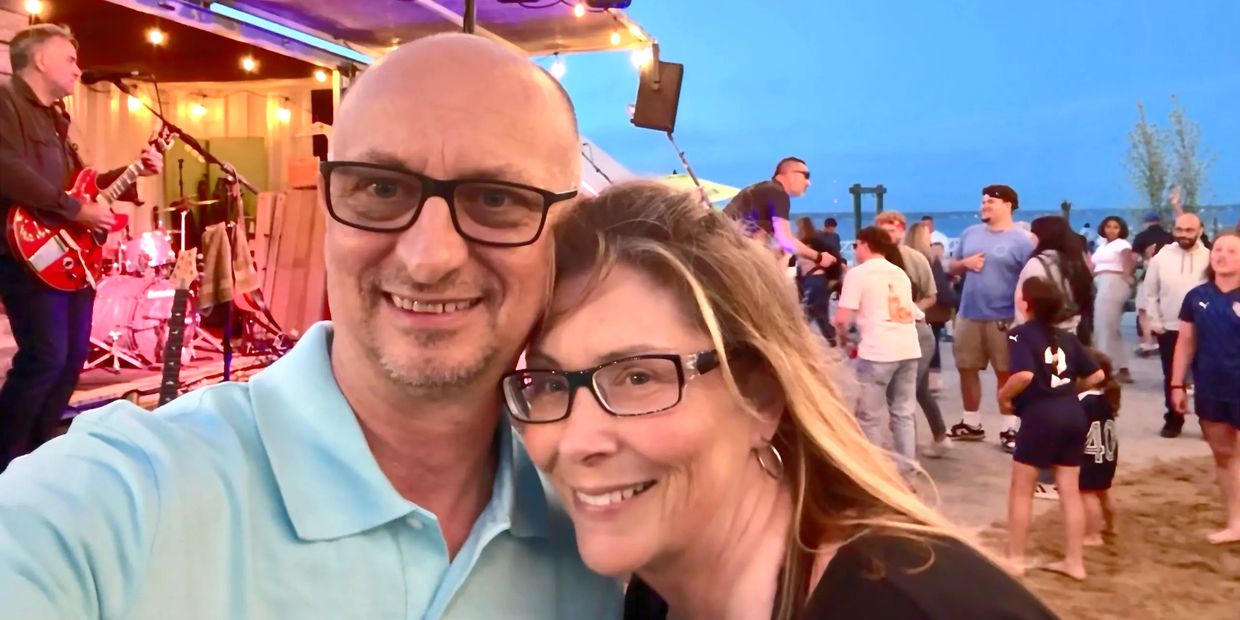 Couple smiling at a beach concert with band and crowd in the background.
