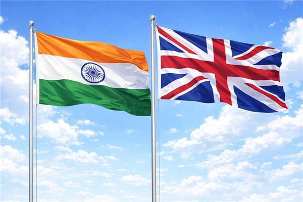 Flags of India and the United Kingdom waving against a blue sky.