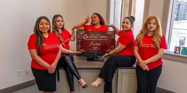 Five women in red shirts posing with a La Doña award plaque.