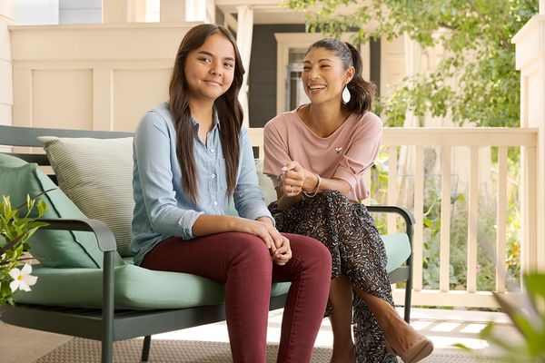 Teenage girl and middle aged woman sitting on a bench outdoors and smiling