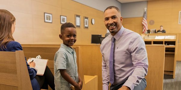 young boy smiling and middle aged man in purple shirt and tie kneeling next to him smiling in court