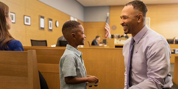 young boy and middle aged man smiling at one another in a court room